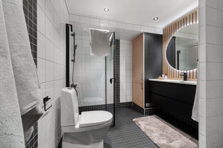 Contemporary bathroom design featuring a clean aesthetic with black and white tiles, a large mirror, and wooden accents.
