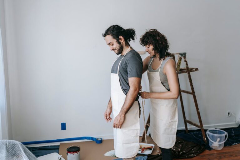 A couple enjoying time together painting a room. They are wearing aprons and working on home renovation.